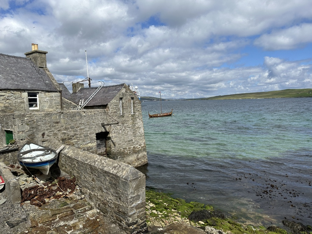 Steinhäuser am Wasser mit Boot vor der Küste auf Shetland