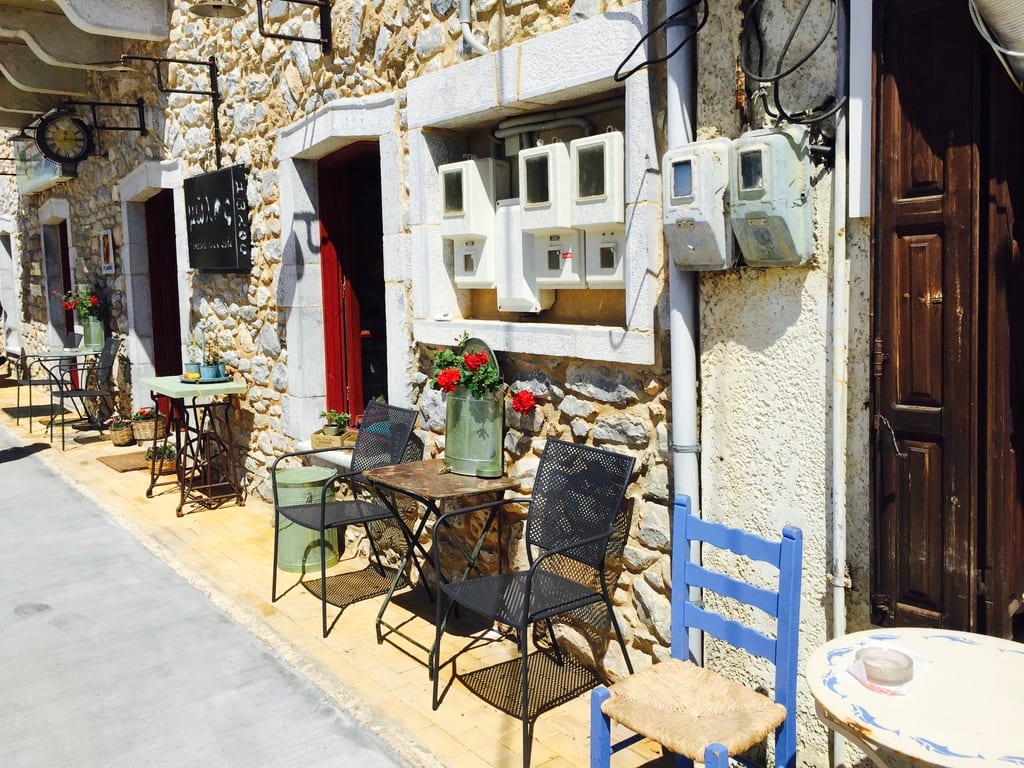 Griechische Gasse mit Café-Tischen und blauem Stuhl