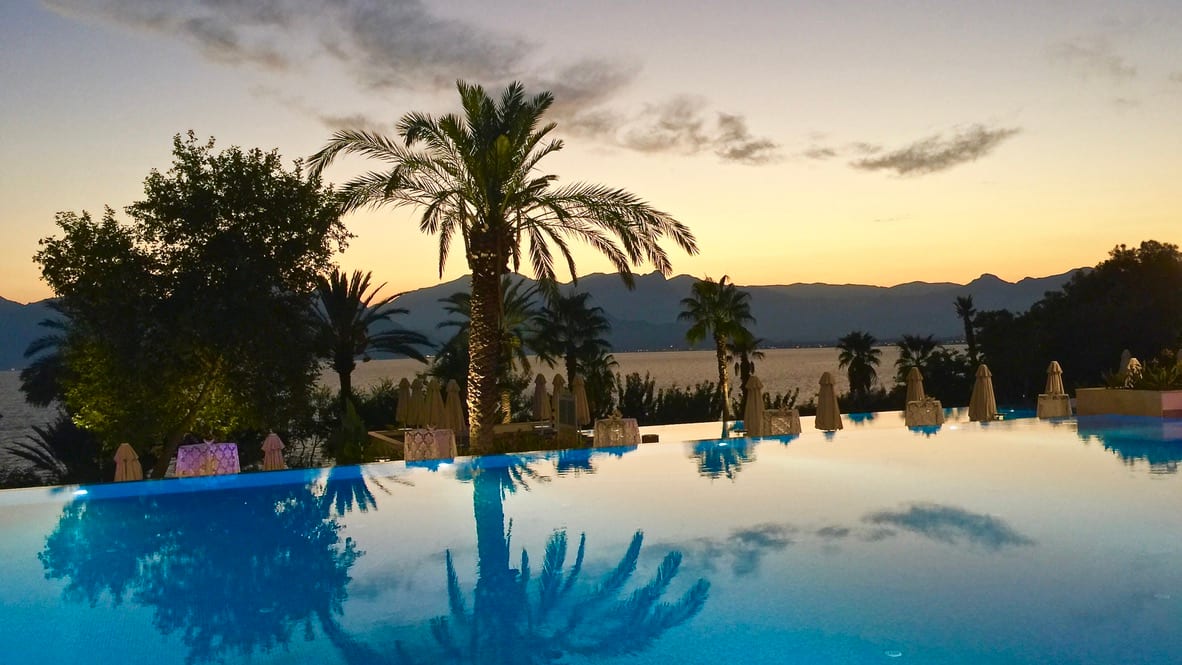 Pool mit Blick auf Meer und Berge bei Sonnenuntergang